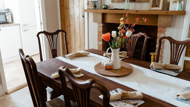 Mesa de jantar posta com cadeiras de madeira, um vaso de flores e um pequeno trem de brinquedo.