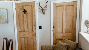 Um quarto com duas portas de madeira, um sofá xadrez, uma cadeira de madeira e um chifre de veado fixado na parede.