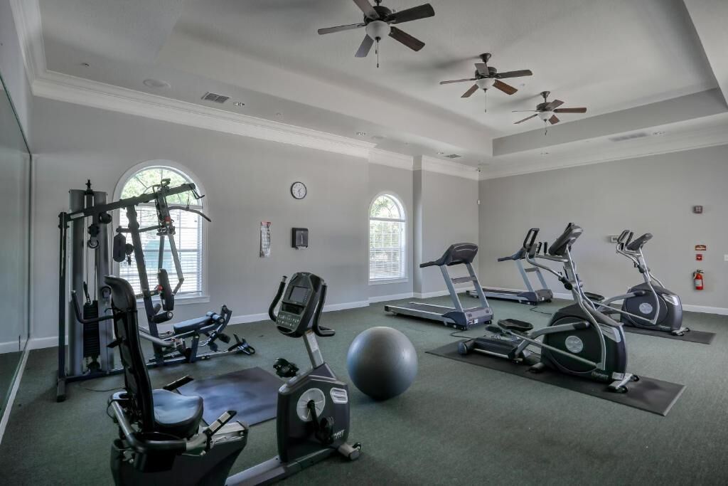 Ein Fitnessstudio mit verschiedenen Trainingsgeräten, darunter Laufbänder, Crosstrainer und Kurzhanteln.