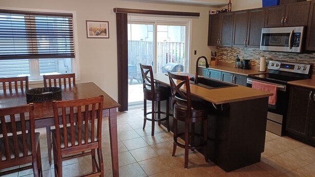Een moderne keuken met een centraal eiland, donkere houten kasten, roestvrijstalen apparatuur en een eetgedeelte met houten stoelen.