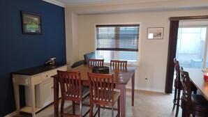 Een eethoek met een houten tafel en stoelen, een raam met zonwering en een keukenblad met kasten.