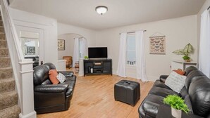 Een moderne woonkamer met een zwarte leren bank, een klein voetenbankje en een flatscreen televisie op een standaard.