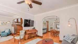 Un salon spacieux avec une table basse en bois, un canapé bleu, une chaise en bois, un téléviseur et un escalier menant à une autre pièce.