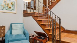 Un escalier avec des marches en bois et des rampes en métal, un fauteuil bleu, une petite table avec une radio, et un tableau encadré représentant des tournesols accroché au mur.