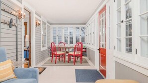 Un couloir étroit abrite un coin repas avec une table et des chaises rouges, bordé de meubles blancs et d’une porte rouge.
