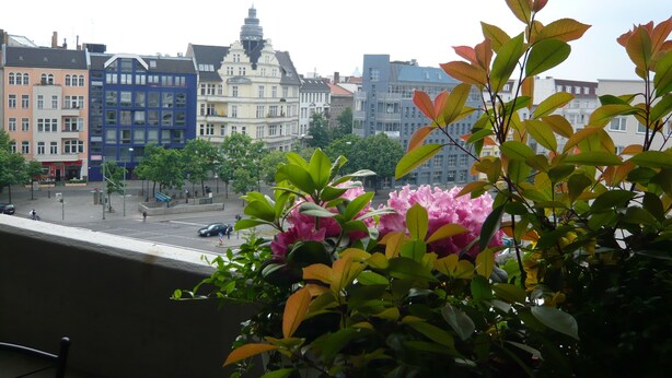 Uma varanda com vista para a paisagem urbana, incluindo edifícios altos e uma rua com carros e pedestres.