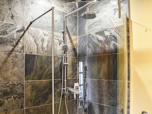 A shower with a glass door, a handheld showerhead, and a wall-mounted faucet.