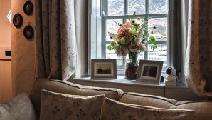 Una habitación acogedora con ventana, un sofá y un florero con flores.