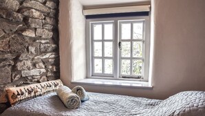 Una cama con colcha, una ventana de marcos blancos y una pared de piedra.