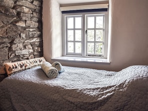 A bed with a quilt, a window with white frames, and a stone wall.