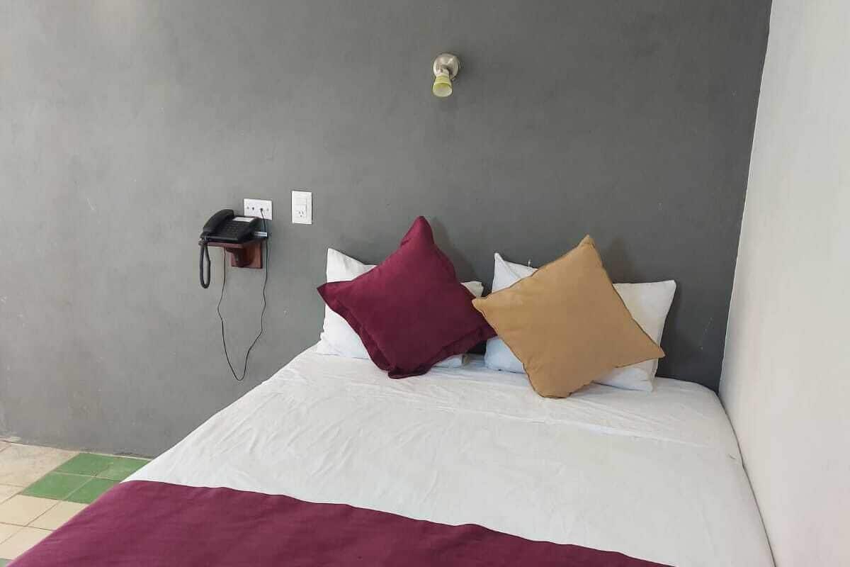 Una cama con colcha blanca y granate, dos almohadas y un teléfono instalado en la pared.