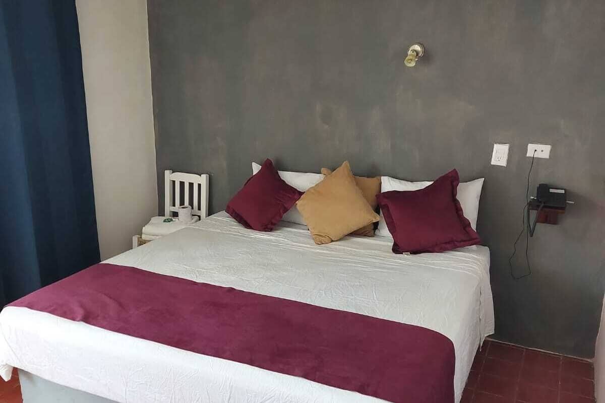 Un dormitorio con cama, almohadas, mesita de noche, toma de corriente e interruptor de pared.