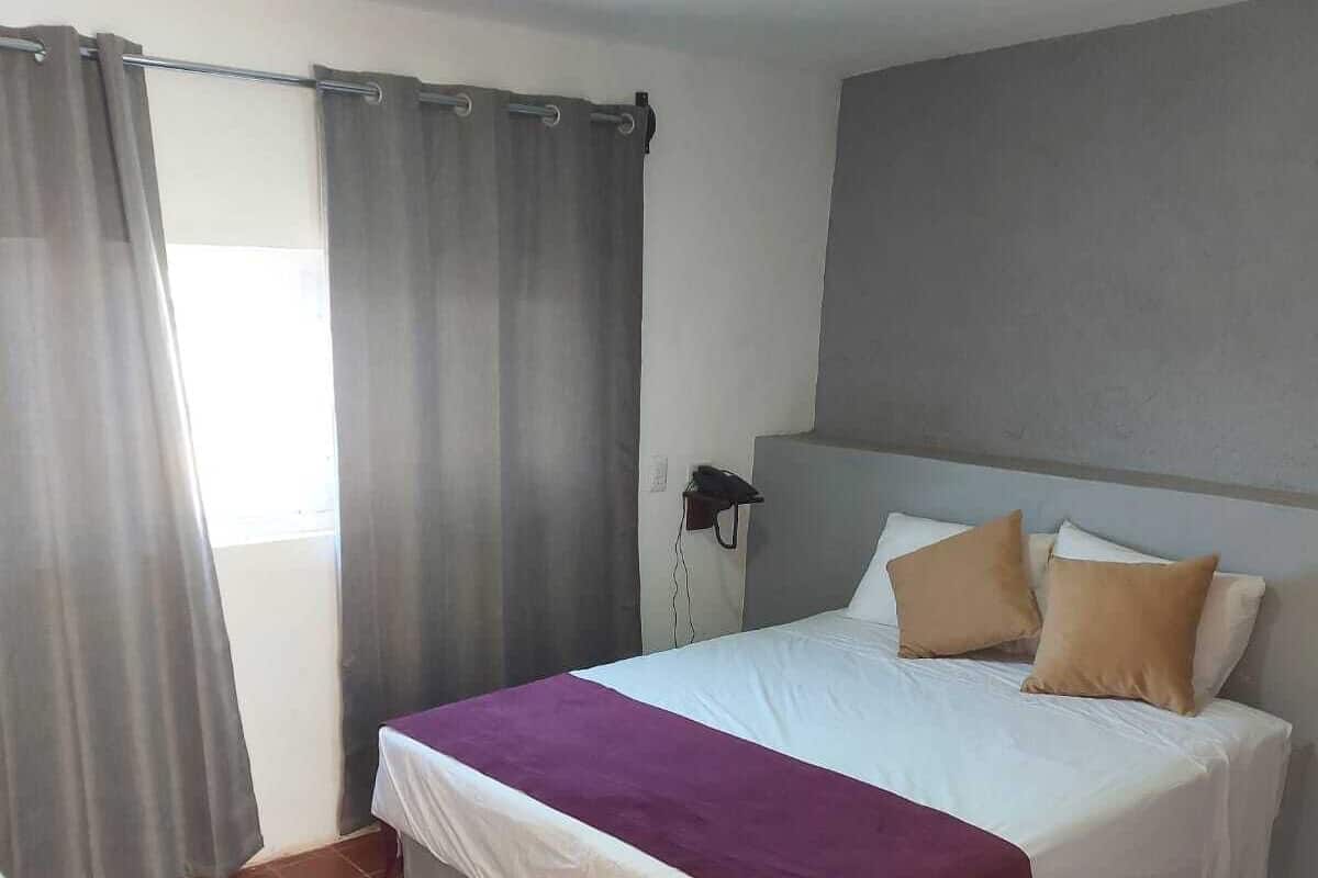 Un dormitorio con cama, cortinas, teléfono junto a la cama y suelo de baldosas.