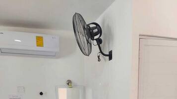 Un baño pequeño con un lavamanos pedestal, un ventilador de pared y una puerta blanca.