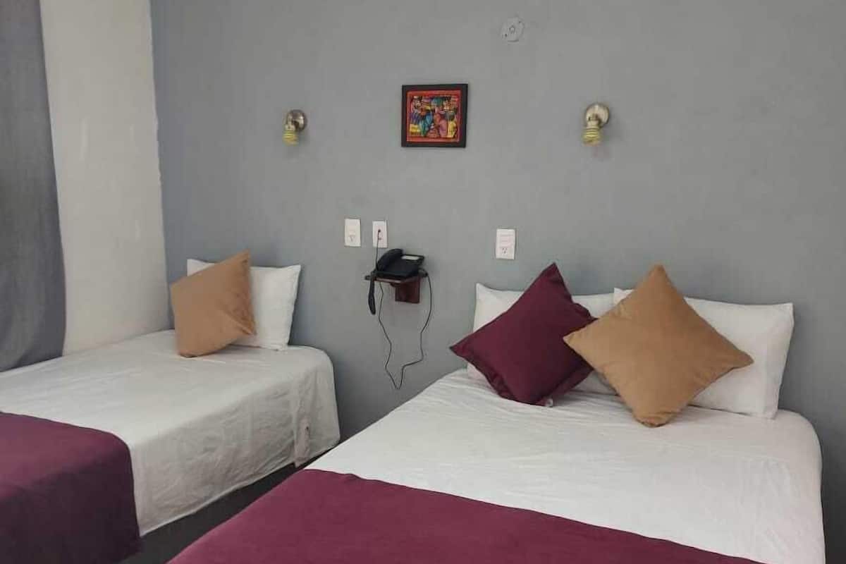 Habitación de hotel con dos camas, cada una con cubrecama blanco y almohadas color burdeos. Hay un cuadro pequeño en la pared, un teléfono y una lámpara.