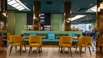 Un intérieur moderne avec un canapé vert, des chaises jaunes et un sol à carreaux.