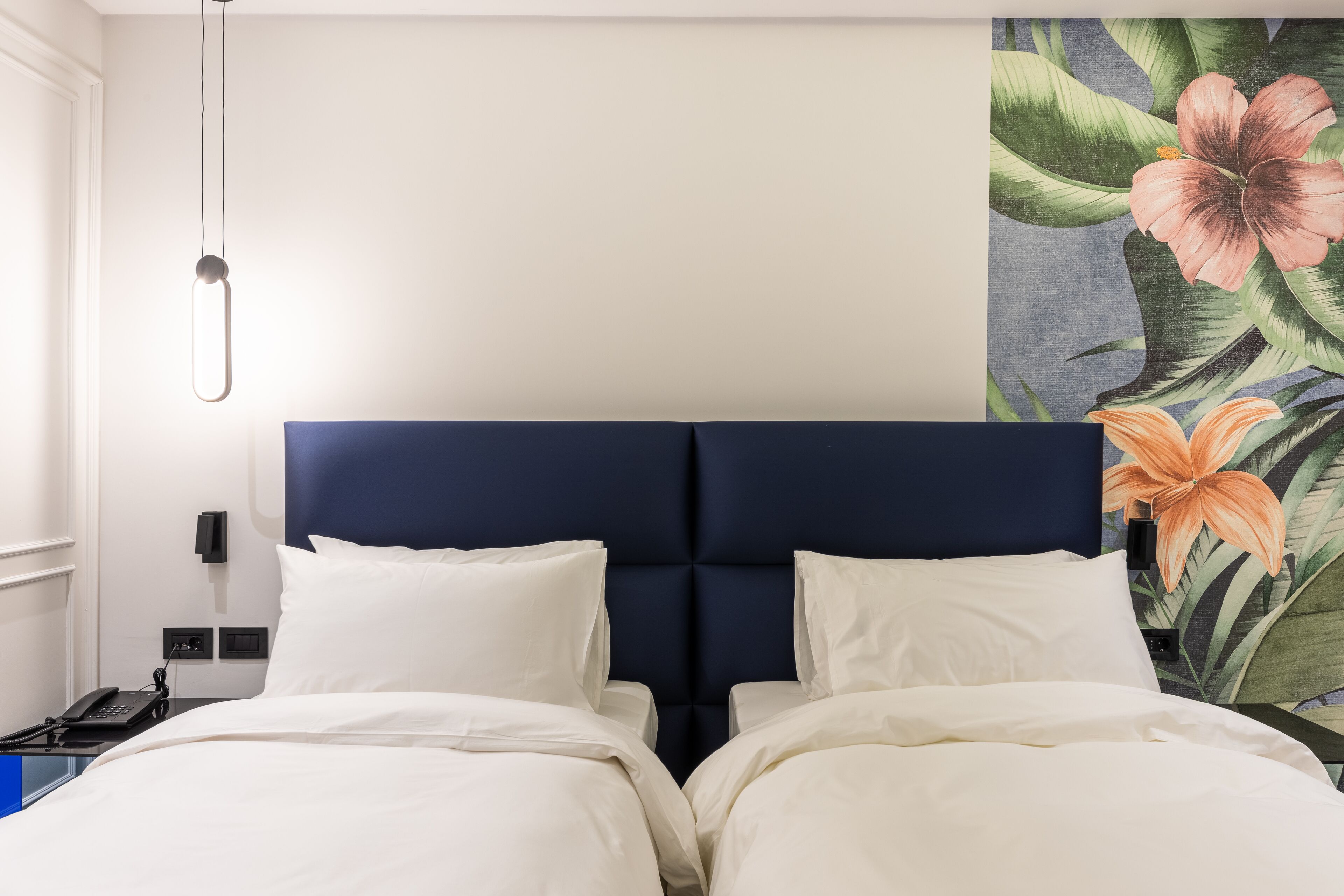 Une chambre d’hôtel avec un grand lit, une tête de lit, une table de chevet, un téléphone et un mur orné d’une fresque florale.