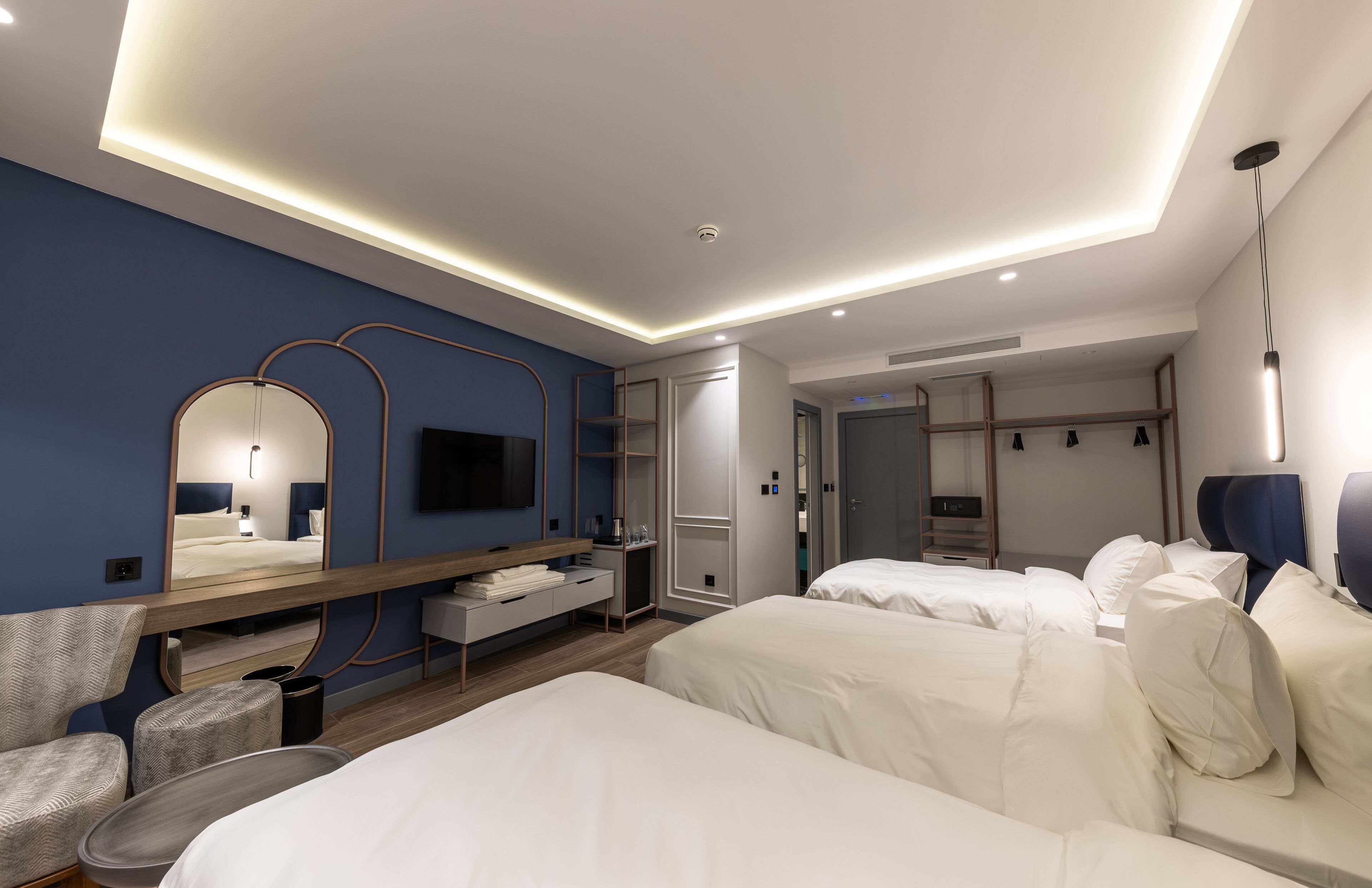 A modern hotel room with a large bed, a desk, a chair, a TV, and a wardrobe.