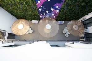 A rooftop terrace with three large umbrellas, a wall with a mural, and a view of the sky.