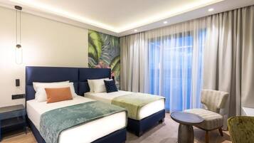Habitació d'hotel amb dos llits, una taula rodona petita, una cadira i una finestra gran amb cortines.