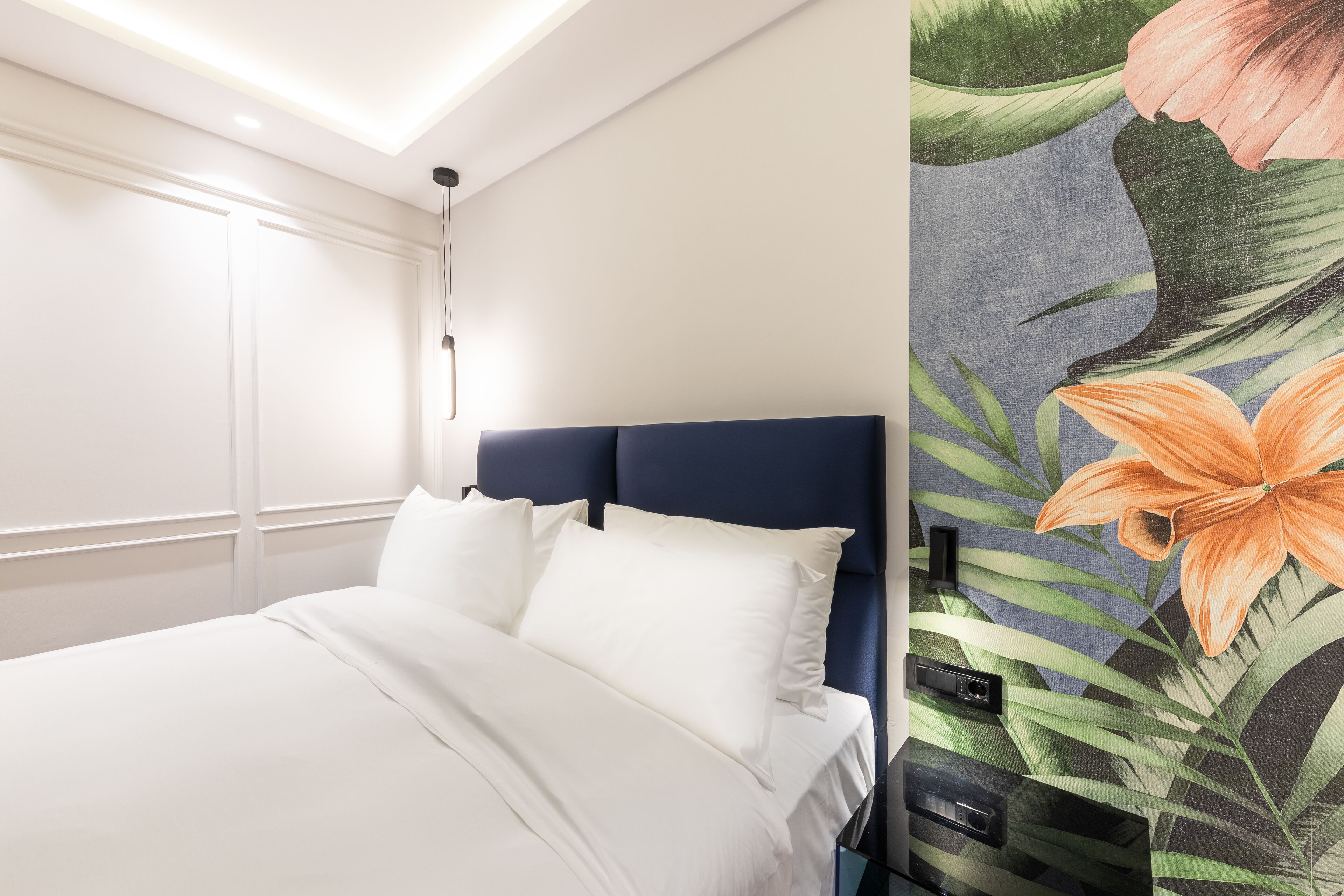 A neatly made bed with white linens, a dark headboard, and a wall with a floral mural.