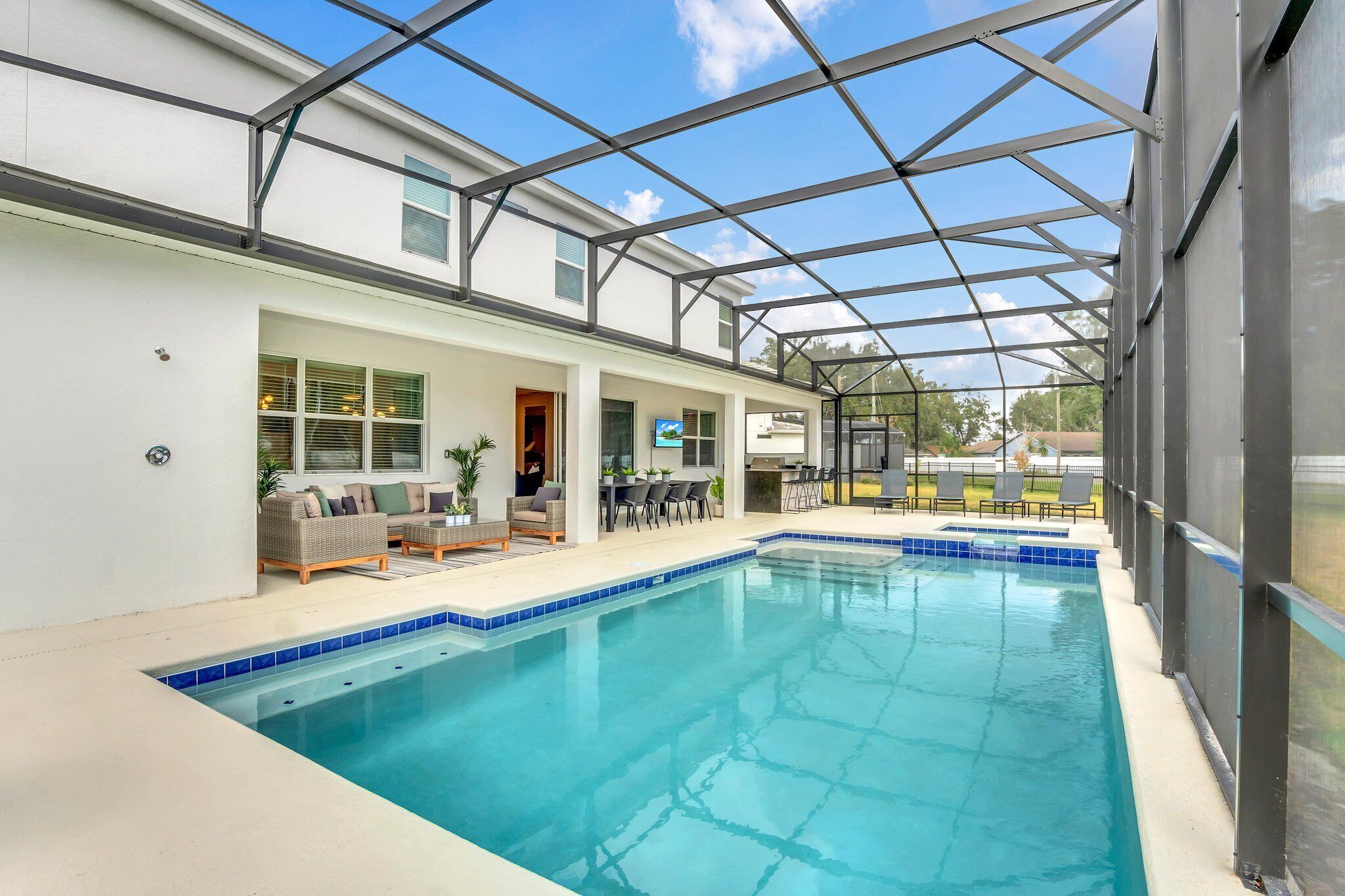 Una piscina cubierta con techo de vidrio, junto a un edificio blanco con un patio y mobiliario exterior.