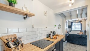 Une cuisine moderne avec un plan de travail en bois, une cuisinière noire et un crédence carrelée blanche. On y trouve un panier de chocolats et une plante sur l’étagère.