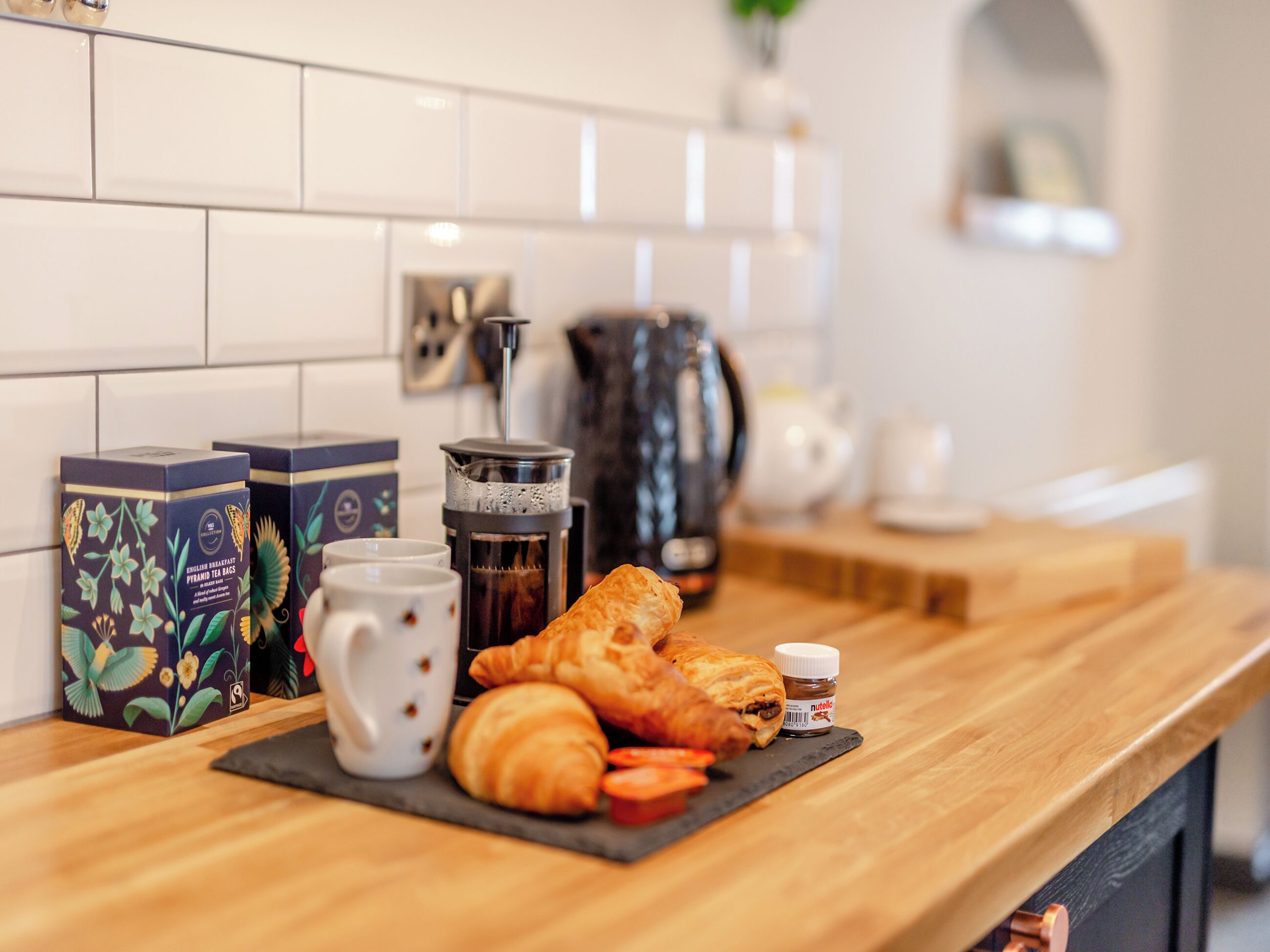 Un comptoir de cuisine avec des aliments pour le petit-déjeuner, notamment des croissants, un pot de Nutella et des sachets de thé.