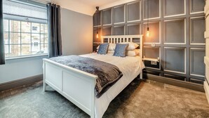 Une chambre à coucher avec un grand lit, une fenêtre avec des rideaux, un luminaire fixé au mur et une bibliothèque intégrée.
