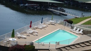 Uma área de piscina com espreguiçadeiras e guarda-sóis, cercada por um deck e um corrimão.