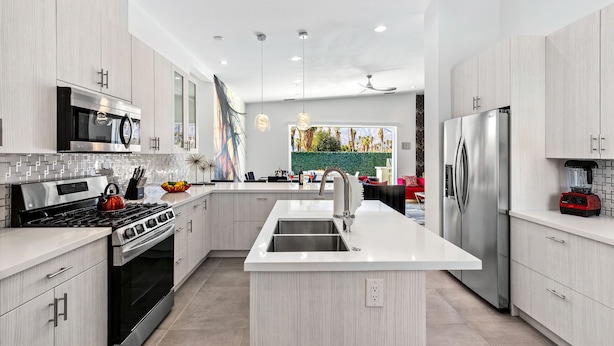 A modern kitchen with stainless steel appliances, a central island, and a view of a landscaped garden. - Picture Perfect Retreat – Modern Hollywood Glam (Palm Springs)