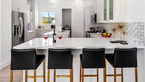 A modern kitchen with a large island, stainless steel appliances, and black bar stools. - Picture Perfect Retreat – Modern Hollywood Glam (Palm Springs)