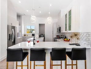 Uma cozinha moderna com uma ilha grande, eletrodomésticos de aço inoxidável e banquetas pretas.