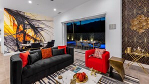 A modern living room with a black and red sofa, a red armchair, a gold side table, and a large abstract painting on the wall. - Picture Perfect Retreat – Modern Hollywood Glam (Palm Springs)