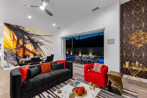A modern living room with a black and red sofa, a red armchair, a gold side table, and a large abstract painting on the wall.