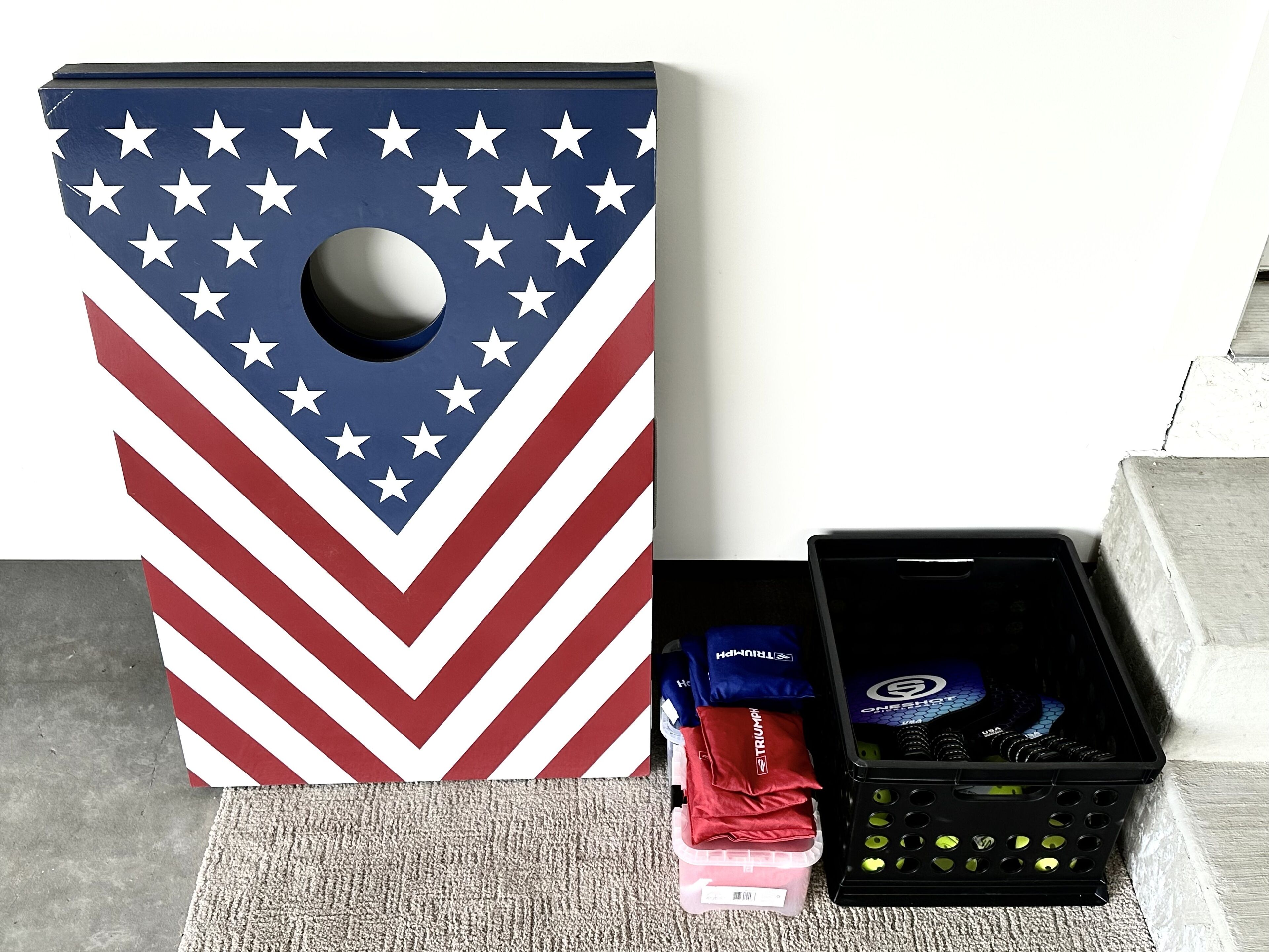 A large American flag-themed dartboard with a black plastic case containing darts and a red and blue bag.