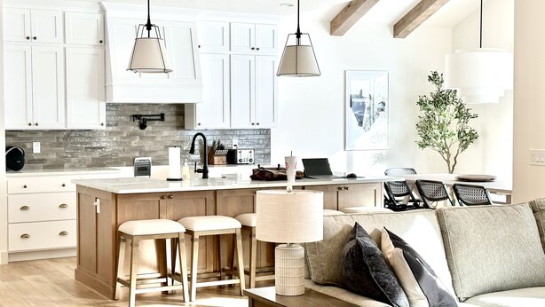 A modern kitchen with white cabinets, a central island with stools, pendant lighting, and a dining area with a sofa and a plant. - New Heber home near Park City. 7brm/5.5ba with hot tub, pickleball, sleeps 18. (Heber City)