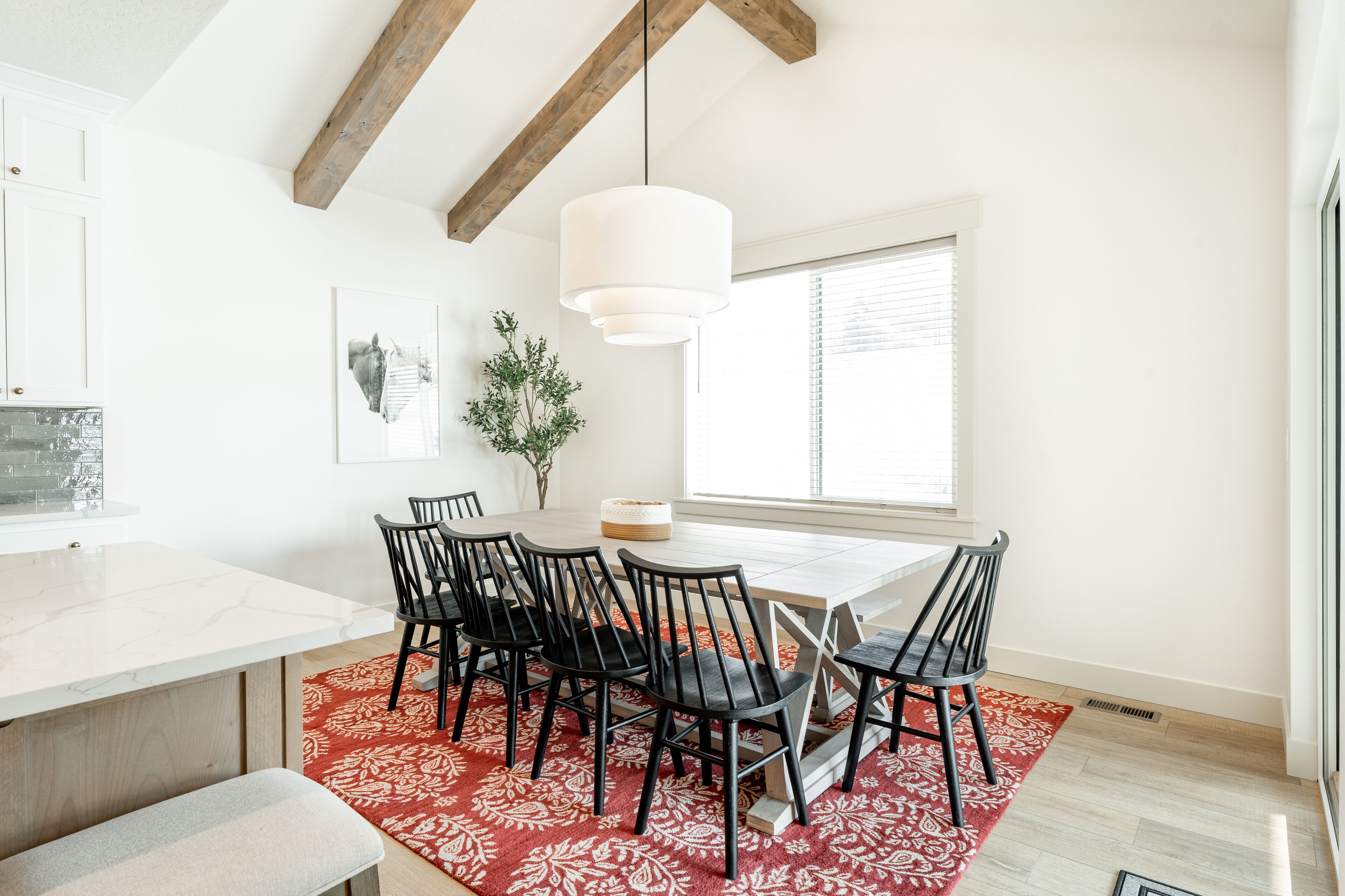 A modern dining area with a white marble table, black chairs, and a red patterned rug.
