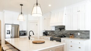 A modern kitchen with white cabinetry, stainless steel appliances, and a large island with bar stools. - New Heber home near Park City. 7brm/5.5ba with hot tub, pickleball, sleeps 18. (Heber City)