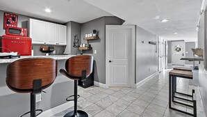 A modern kitchen with white cabinets, a red appliance, and two wooden bar stools. - Relaxing Retreat  (Westminster)