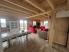 Ein Interieur einer Holzhütte mit Essbereich, roten Stühlen, einem Fernseher und einem großen Fenster mit Blick auf eine reizvolle Landschaft.