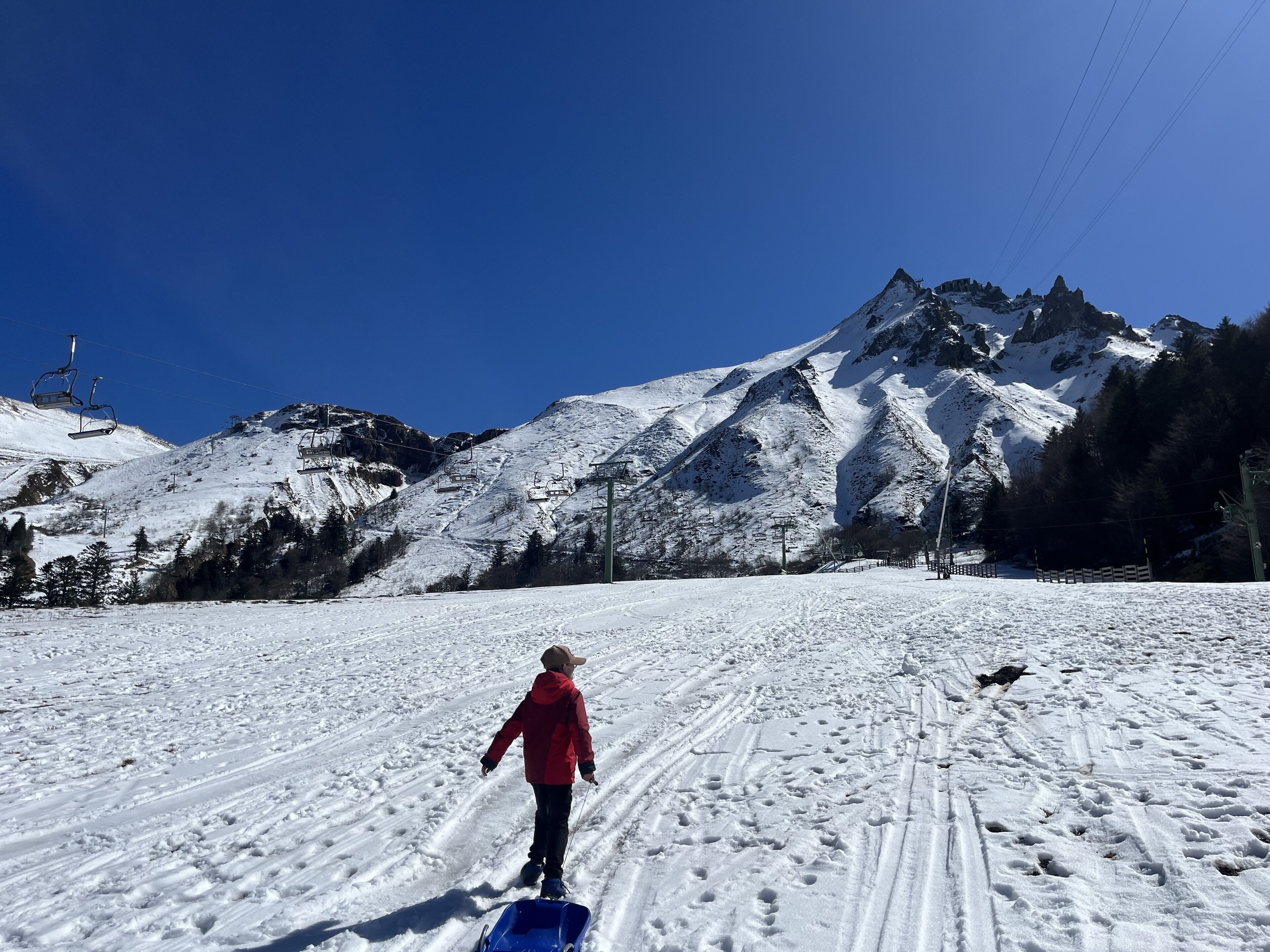 A snowy mountain slope with ski lifts and a child sledding.