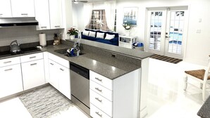 A modern kitchen with white cabinetry, a granite countertop, a dishwasher, and a blue sofa in the dining area.