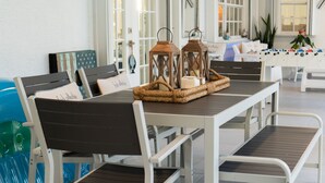 A dining area with a long table, white chairs, and a wicker tray with candles.