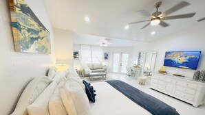 A modern bedroom with a large bed, a desk, a chair, a TV, and a ceiling fan.
