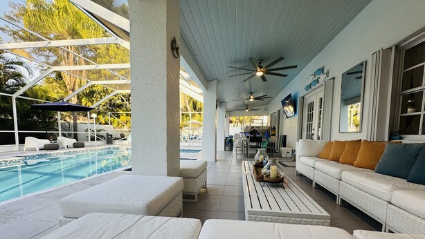 A covered outdoor area with a pool, white furniture, ceiling fans, and a view of the pool.