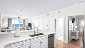 A modern kitchen with white cabinetry, a built-in dishwasher, and a large island with a sink.