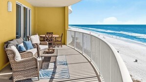 A balcony with wicker furniture, a table, and a view of the beach.