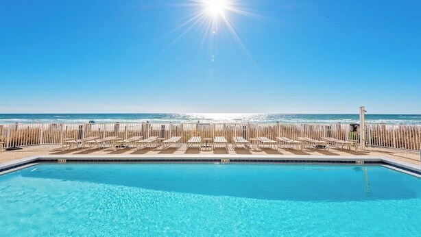 A pool with clear blue water, a wooden fence, and a beach view.
