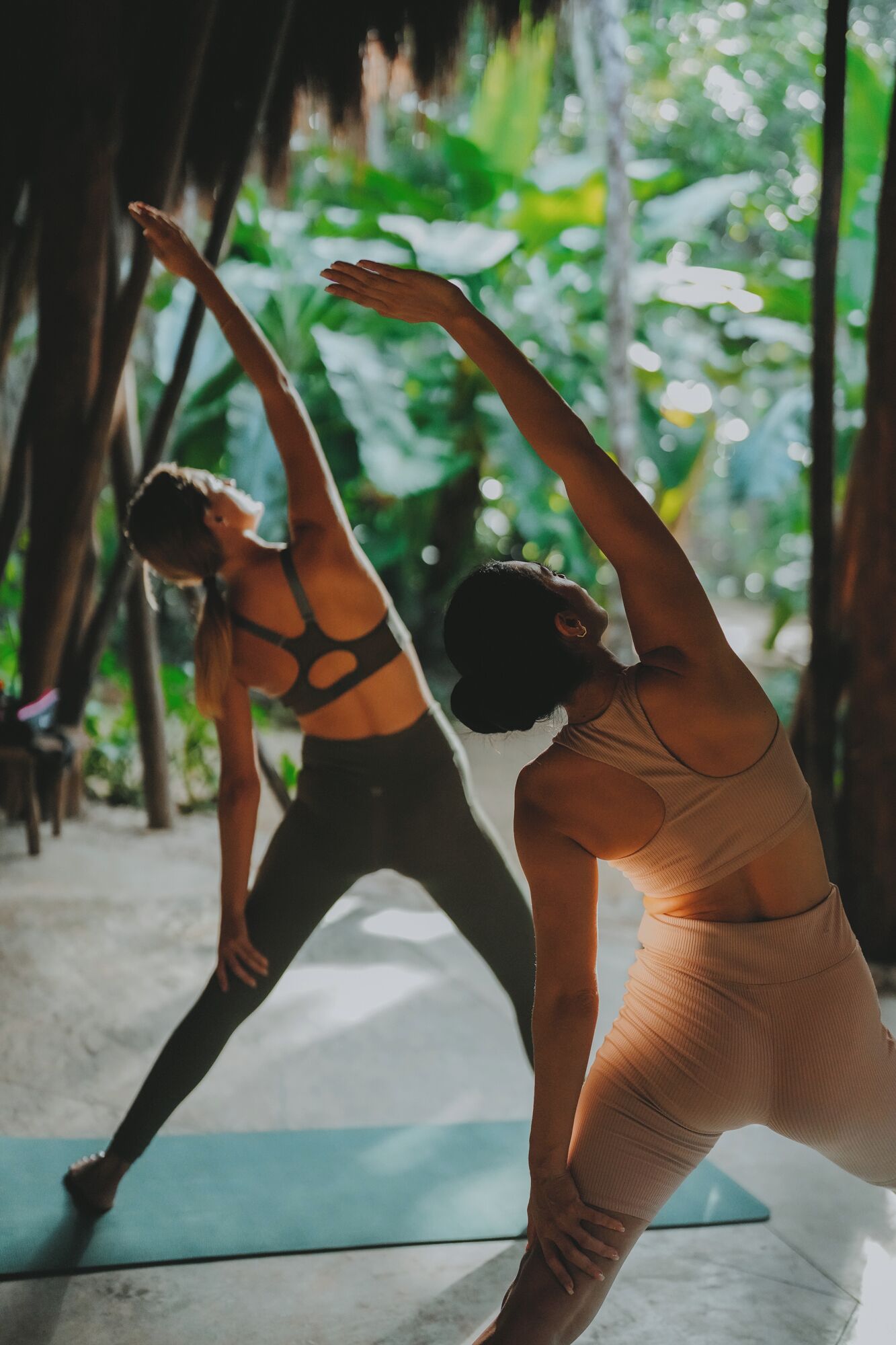 Dos personas practicando yoga en una habitación con vistas a zonas verdes.